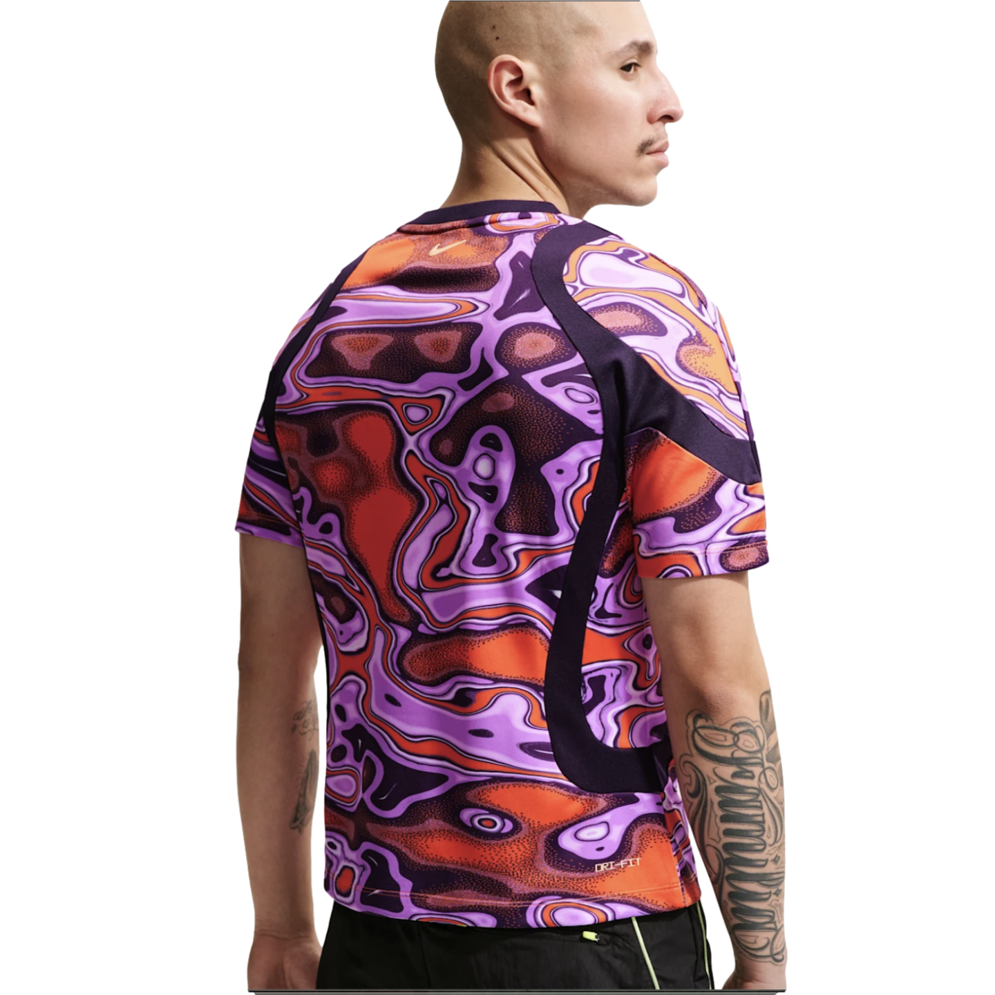 Rear view of a man wearing a Nike shirt with a vibrant, abstract purple and orange pattern. He has a bald head and arm tattoos, set against a plain white background.