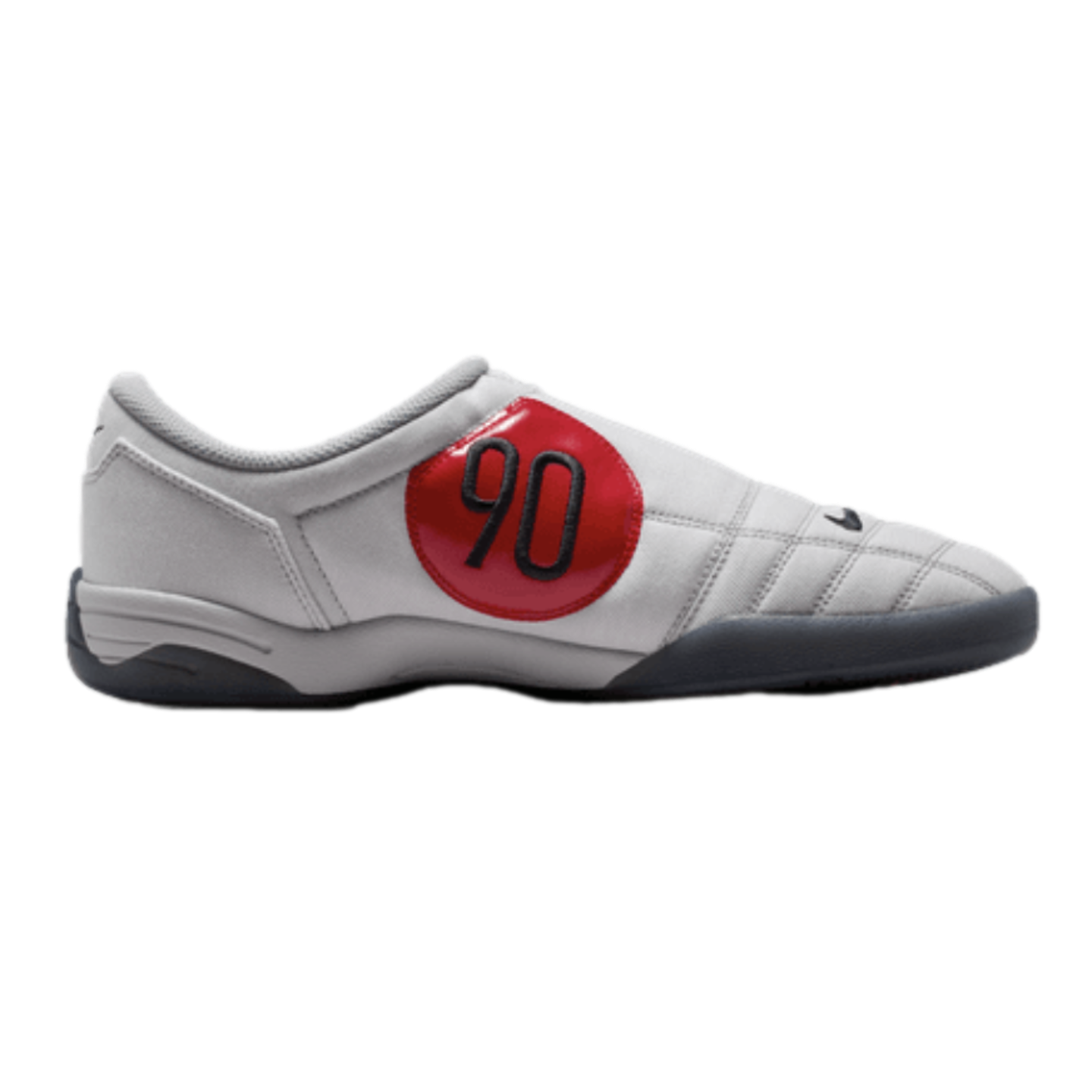 Side profile of a grey Nike Total 90 indoor soccer shoe with a large red circular patch featuring a black "90" and a dark grey sole.