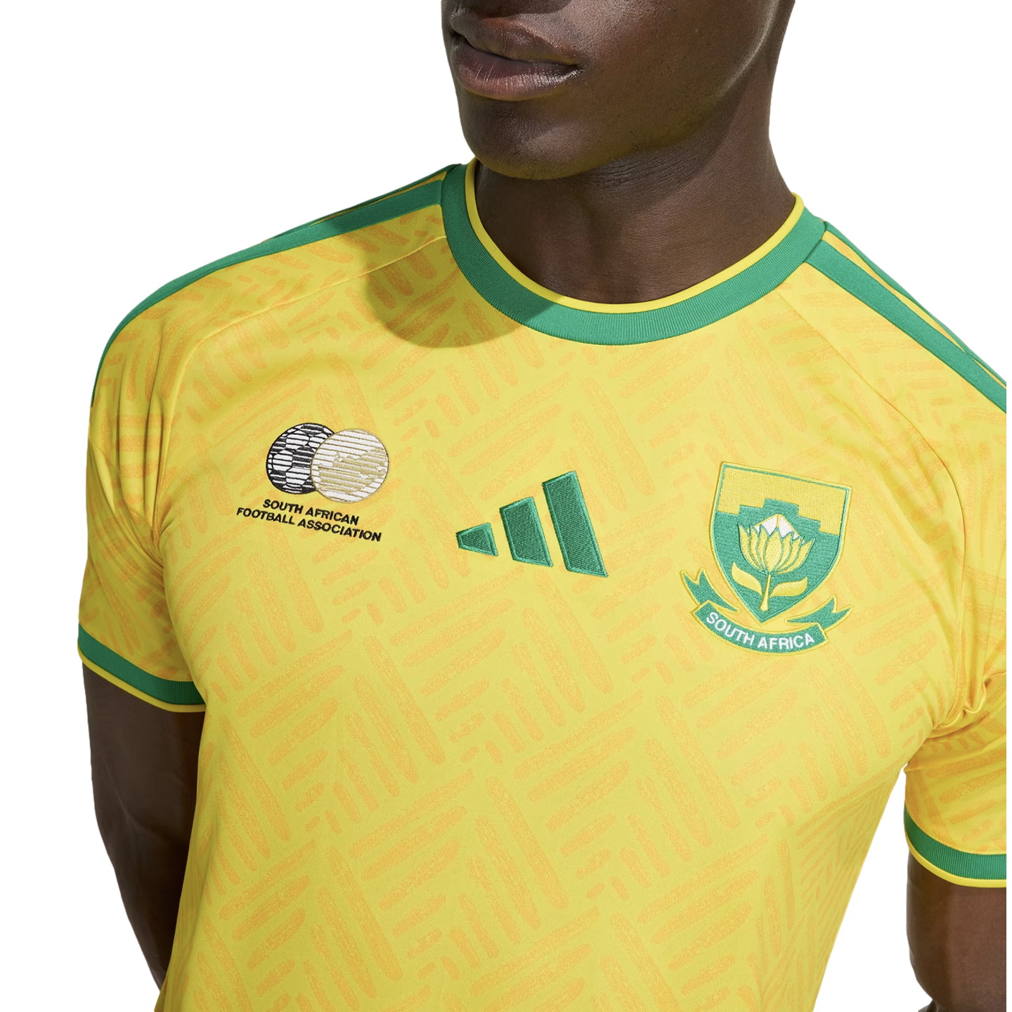 Close-up of a person wearing a yellow South Africa national football team jersey with green accents, featuring the Adidas logo and team crests.