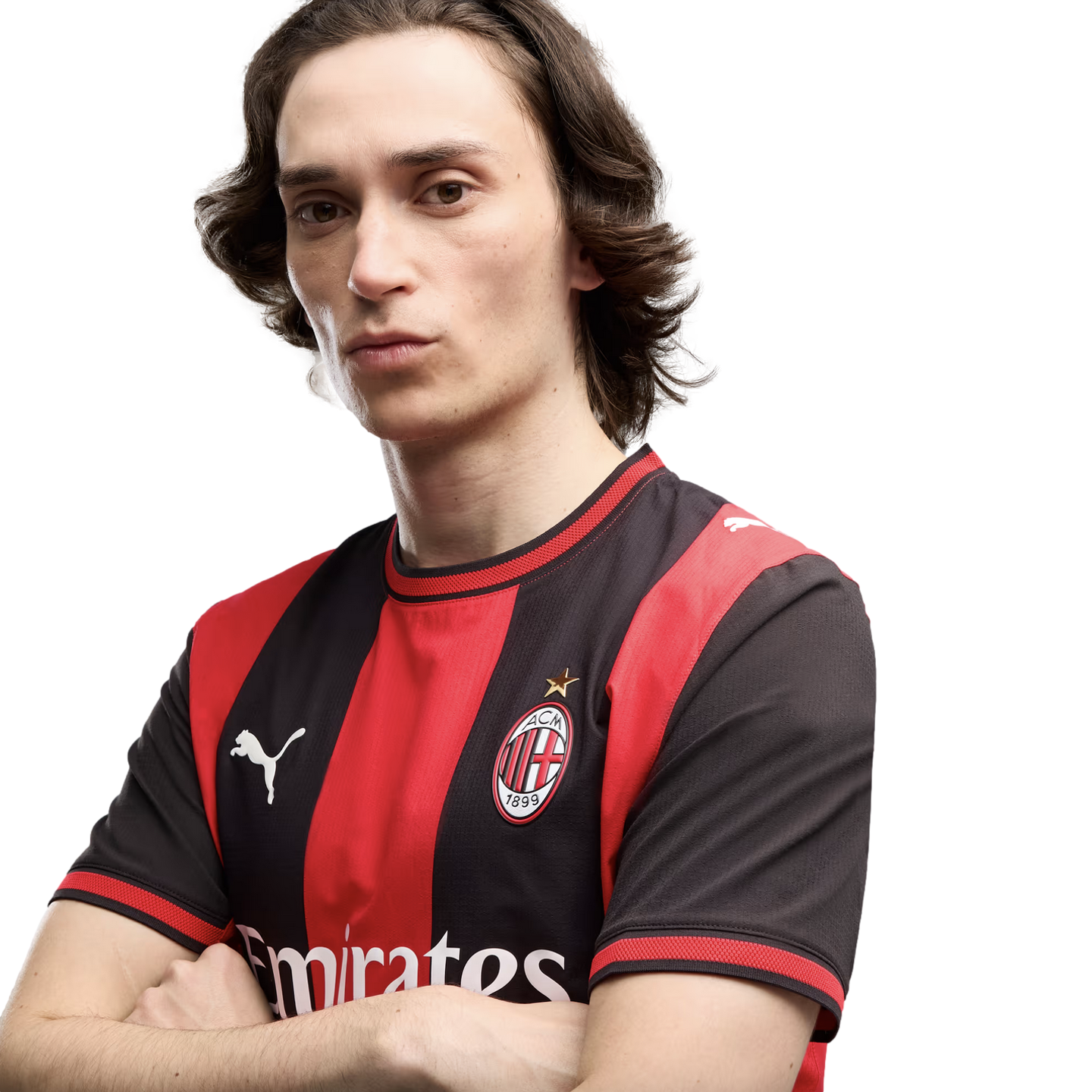 A man with shoulder-length brown hair and arms crossed, wearing a red and black AC Milan soccer jersey with a white Puma logo against a plain white background.