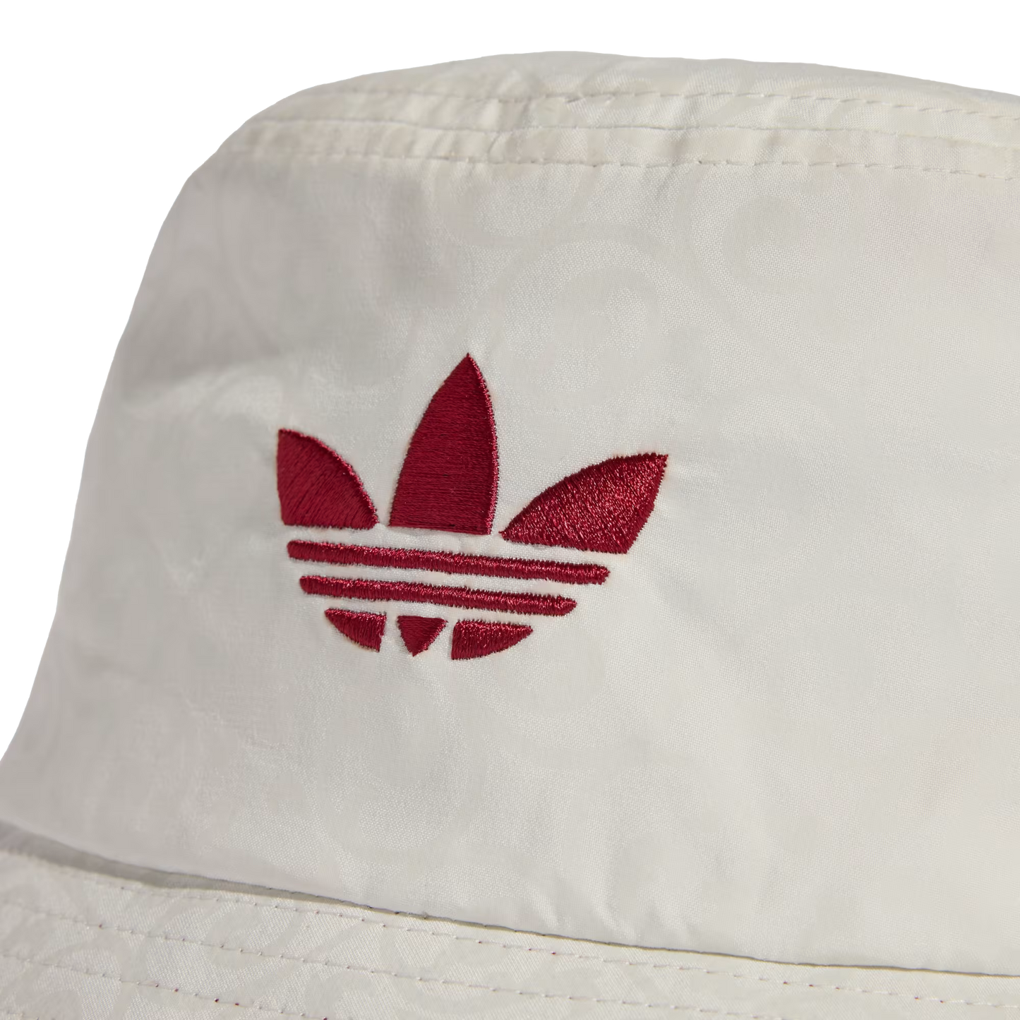 A close-up of a white bucket hat featuring a red embroidered Adidas trefoil logo on the front crown. The fabric has a subtle, repeating tonal pattern weave.