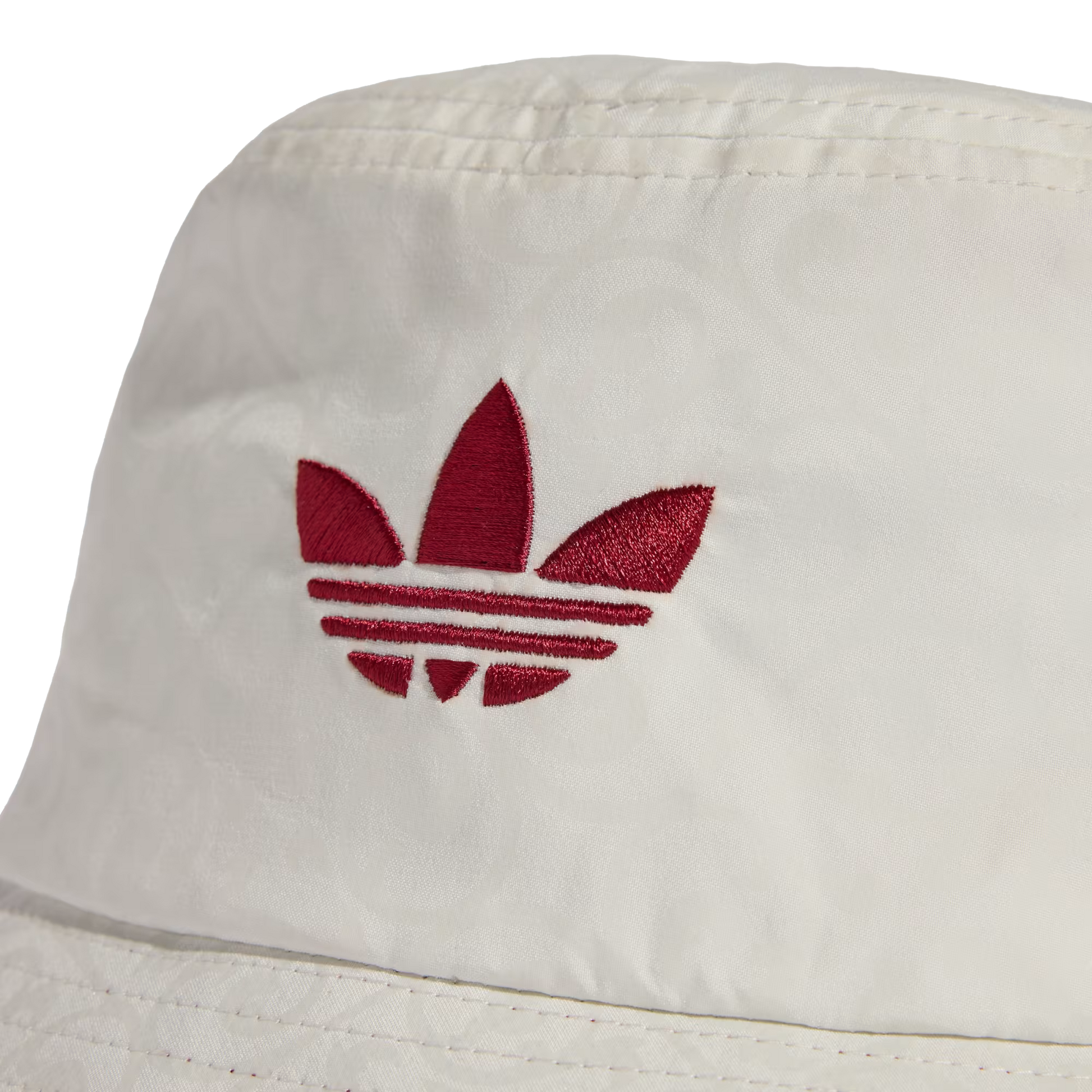 A close-up of a white bucket hat featuring a red embroidered Adidas trefoil logo on the front crown. The fabric has a subtle, repeating tonal pattern weave.